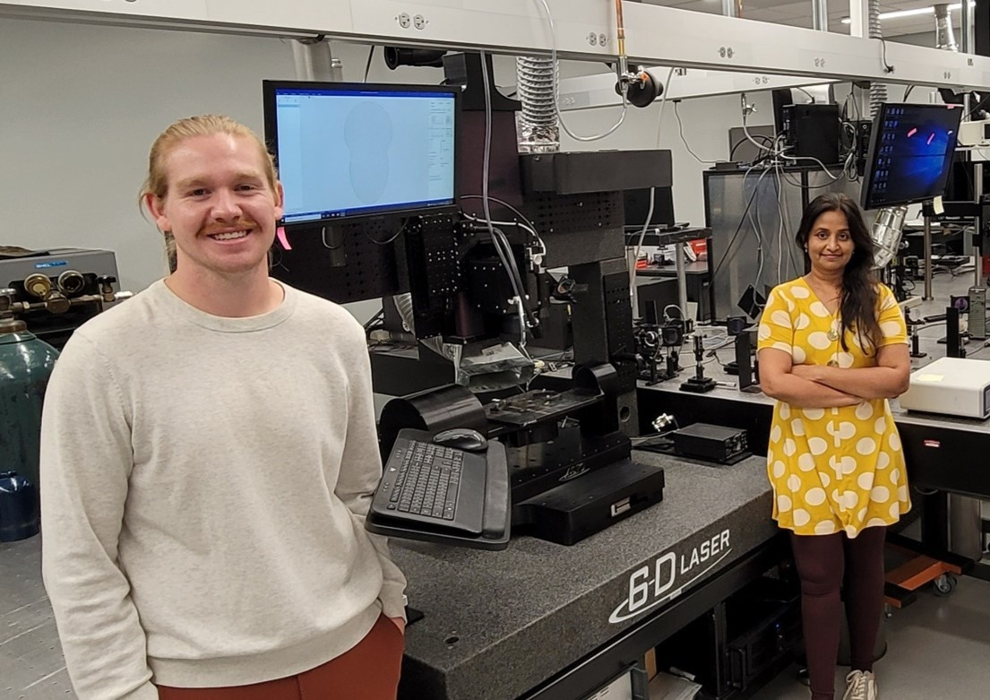 Two researchers standing next to a piece of equipment in a lab